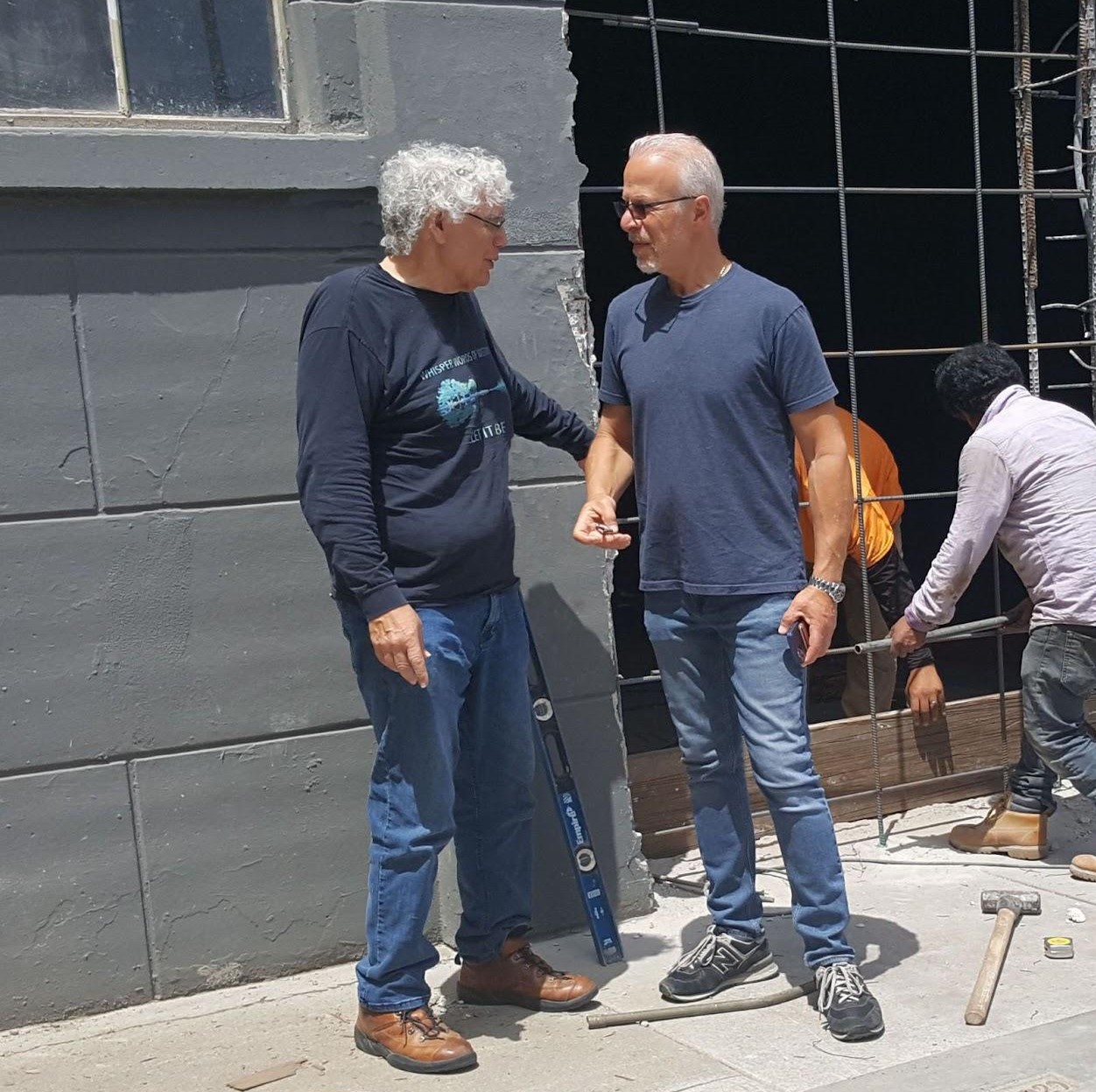 Martin Espinosa consulting on a job site with a client. They are standing outside in deep discussion with two working behind them - Crystal Construction Consulting